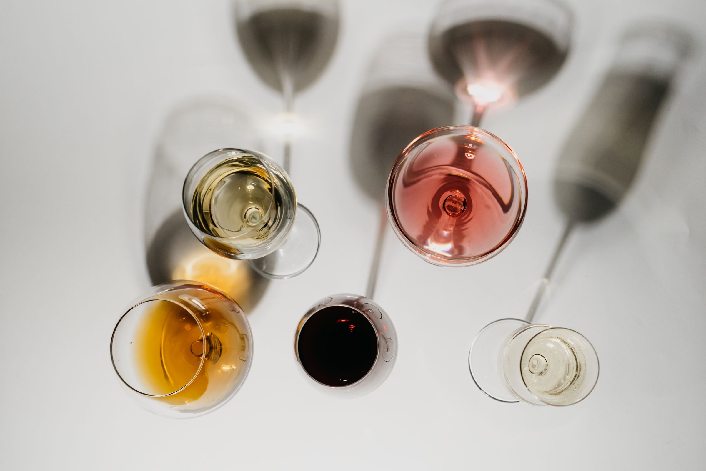 Overhead view of five glasses holding different styles of wine, from pale white and rosé to deep red and amber
