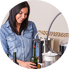 Smiling woman holding a green bottle under a countertop bottle filler in her kitchen