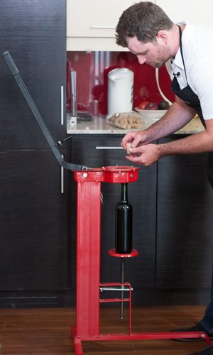 A red floor-standing corker with a wine bottle in the cradle and a winemaker reaching for a cork