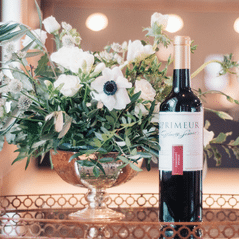 Bottle of En Primeur red wine on a mirrored table beside a footed bowl of white anemones