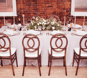 Long wedding table set with bottles of wine, tapered candles and a garland of white flowers in a brick hall