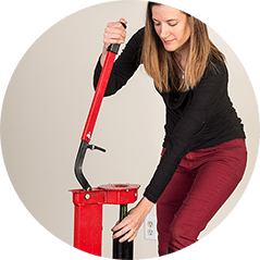 A woman pressing down the lever of a red floor corker to cork a wine bottle